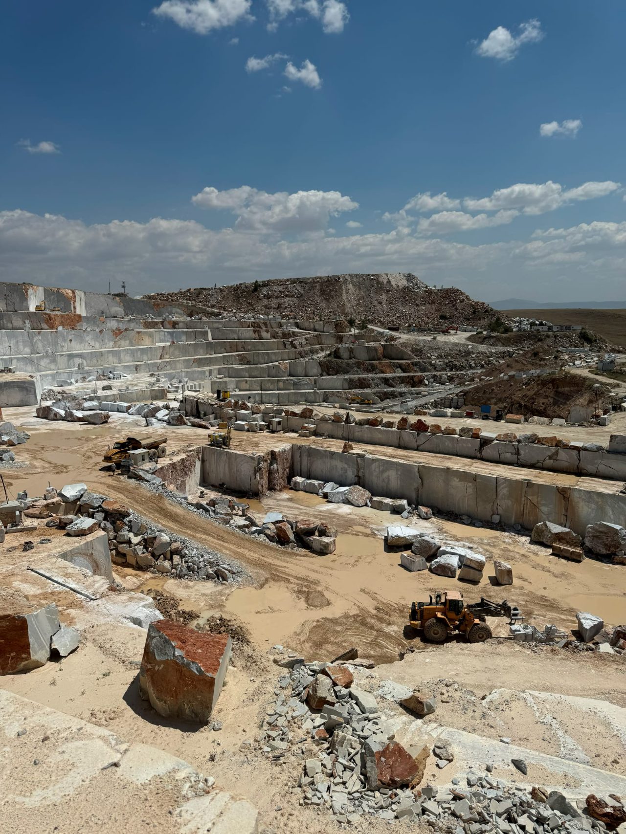 Terraced open-pit stone quarry with cut blocks, loaders and quarry roads under a blue sky